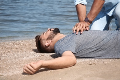 Photo of Passerby performing CPR on unconscious young man near sea. First aid