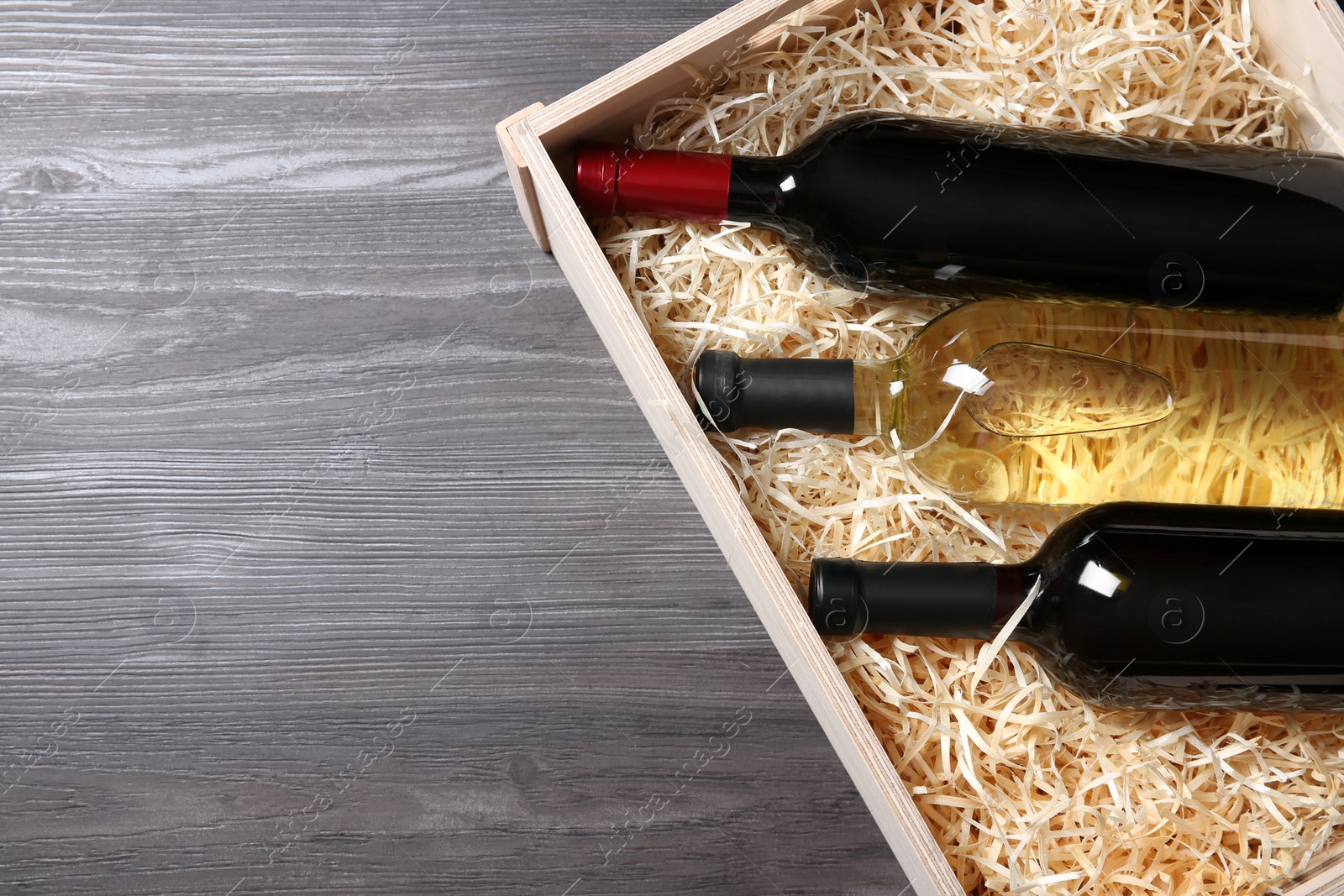 Photo of Wooden crate with bottles of wine on grey table, top view. Space for text