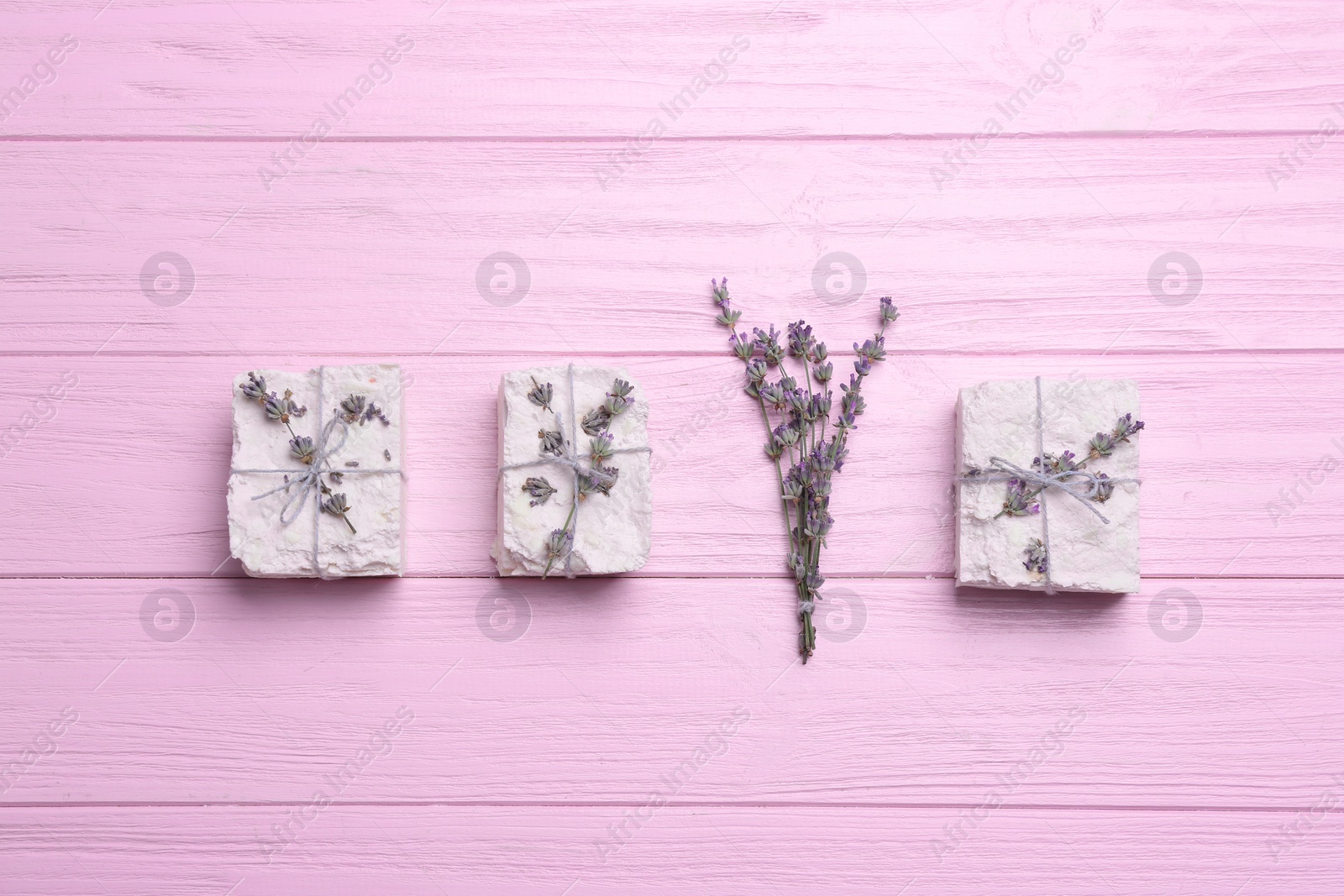 Photo of Hand made soap bars with lavender flowers on pink wooden table, flat lay