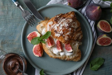 Photo of Delicious croissant with figs and cream served on light blue wooden table, flat lay