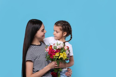 Photo of Happy woman with her daughter and bouquet of beautiful flowers on light blue background, space for text. Mother's day celebration