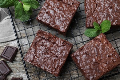 Cooling rack with delicious chocolate brownies and fresh mint on wooden table, flat lay