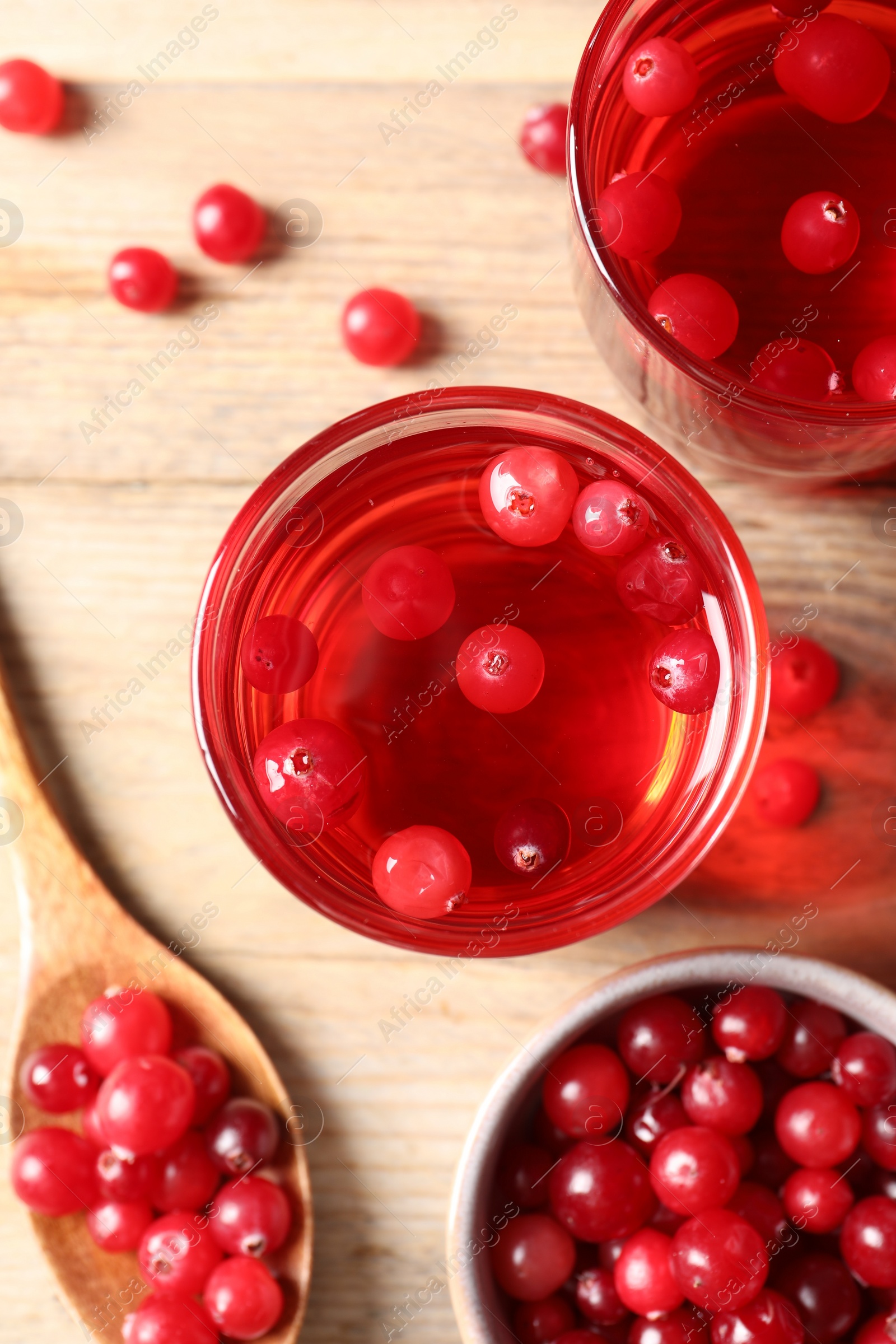 Photo of Tasty cranberry juice in glasses and fresh berries on wooden table, flat lay