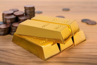 Photo of Stacked gold bars and coins on wooden table