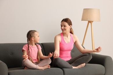 Photo of Mother with daughter meditating on sofa indoors. Harmony and zen