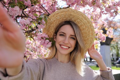 Happy woman taking selfie near blossoming sakura outdoors on spring day