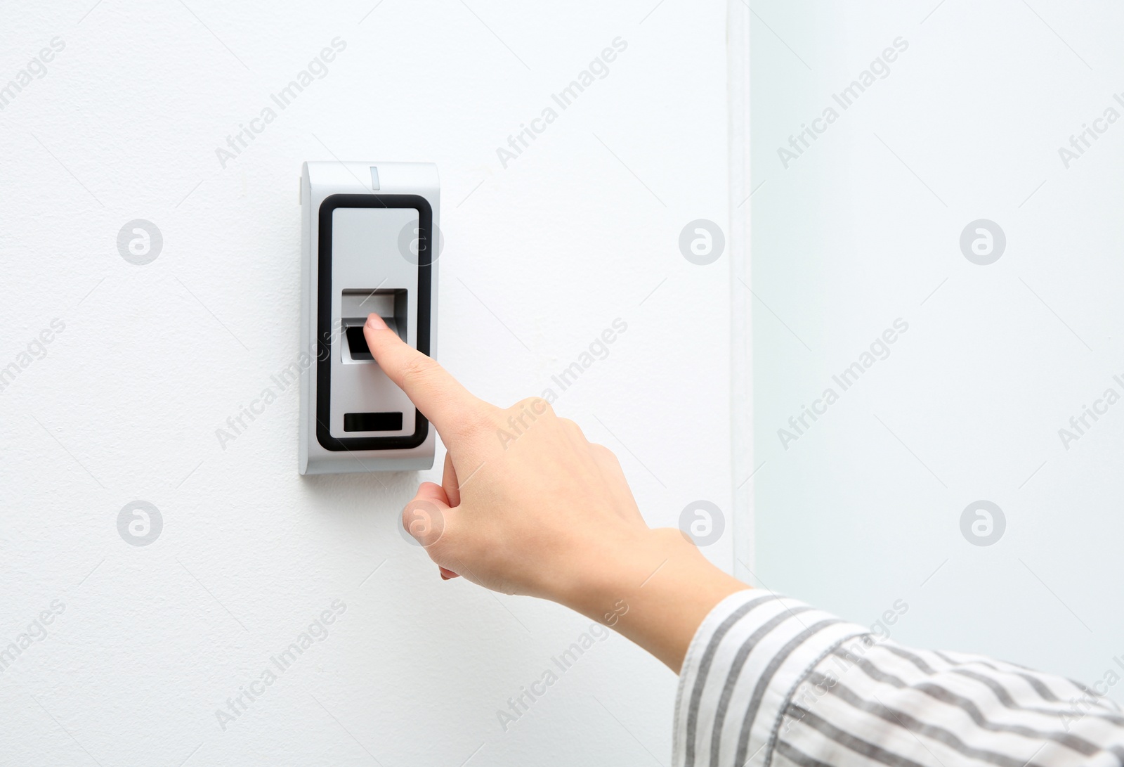 Photo of Young woman pressing fingerprint scanner on alarm system indoors