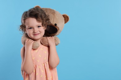 Cute little girl with teddy bear on light blue background, space for text