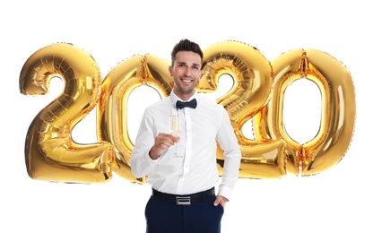 Happy young man with glass of champagne near golden 2020 balloons on white background. New Year celebration