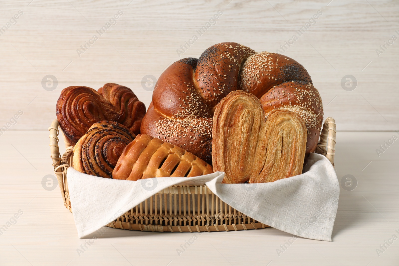 Photo of Wicker basket with different tasty freshly baked pastries on white table