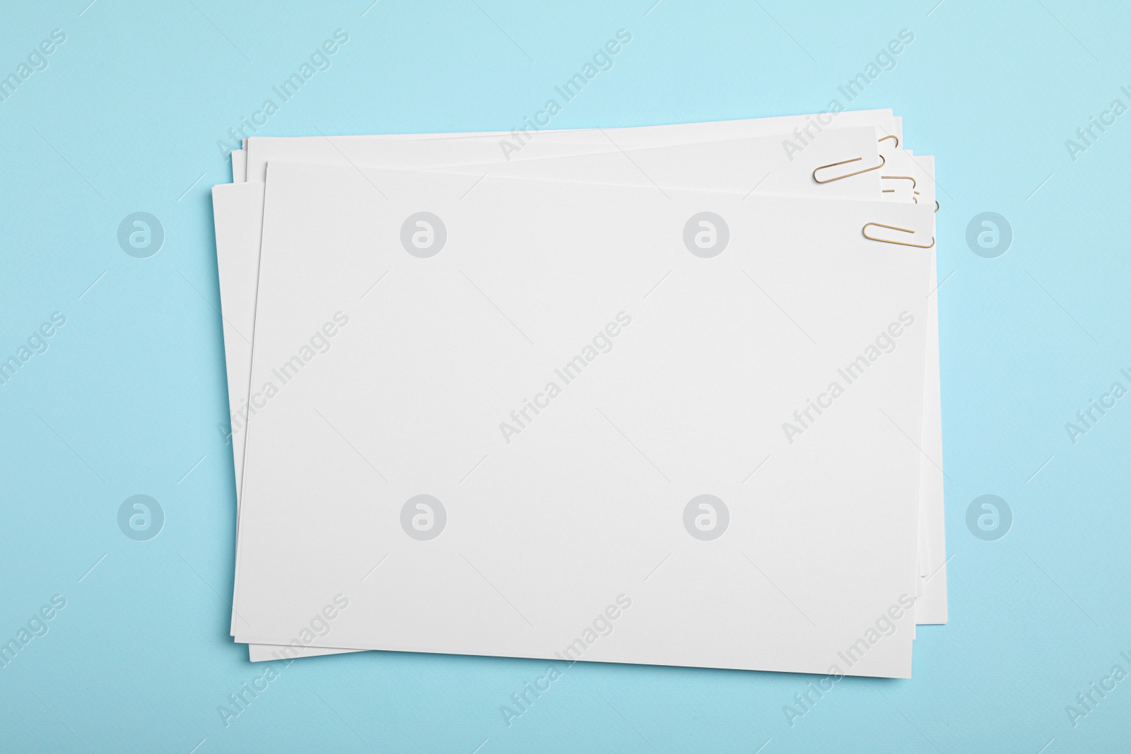 Photo of Sheets of paper with clips on light blue background, top view