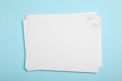 Photo of Sheets of paper with clips on light blue background, top view