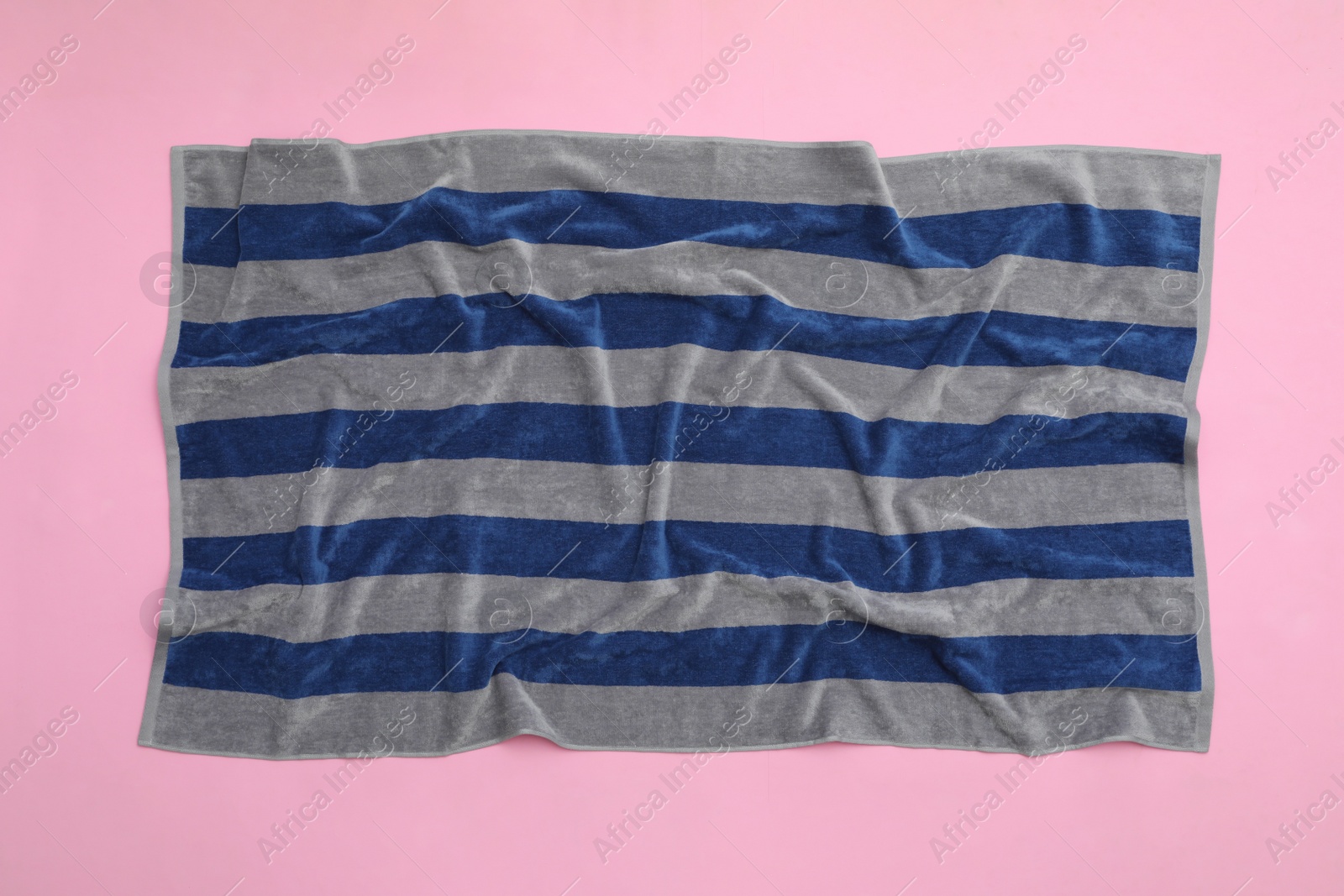 Photo of Crumpled striped beach towel on pink background, top view