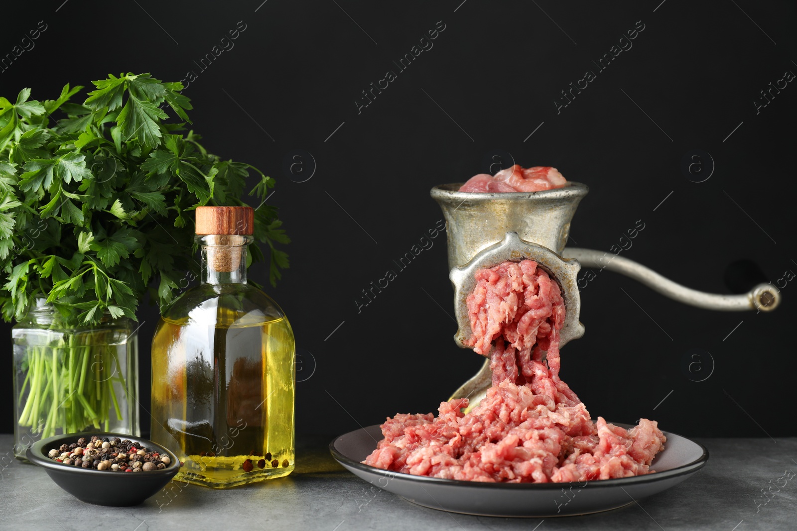 Photo of Manual meat grinder with beef mince, spices, oil and parsley on grey table