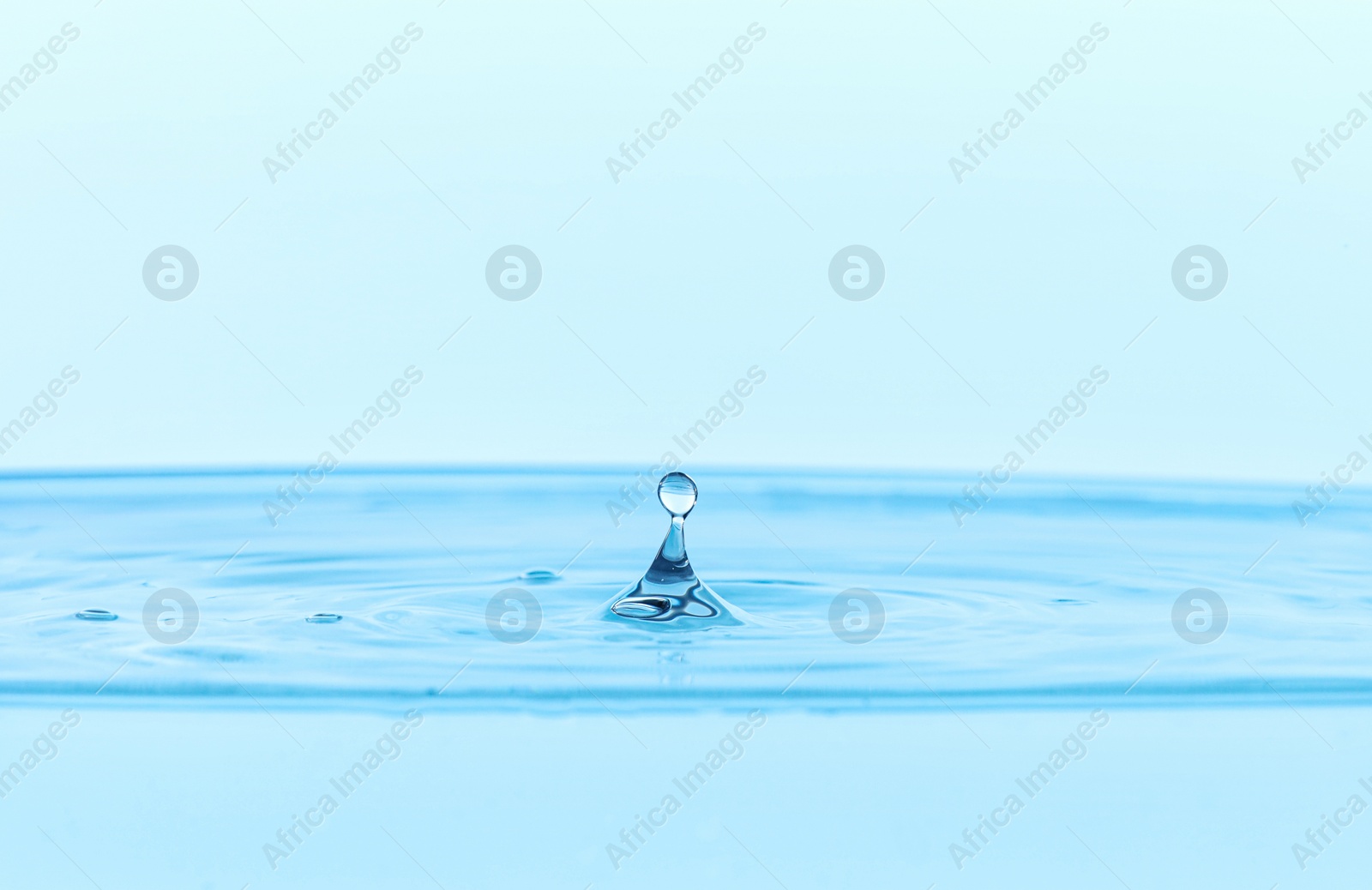 Photo of Splash of clear water with drop on light blue background, closeup