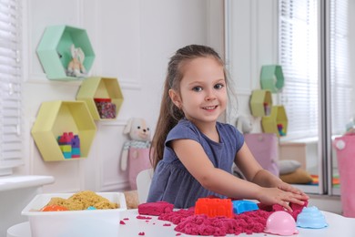 Photo of Cute little girl playing with bright kinetic sand at table in room