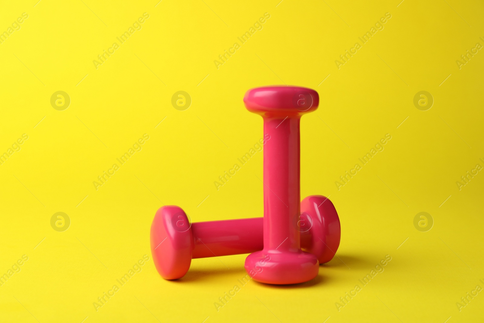 Photo of Two stylish pink dumbbells on yellow background