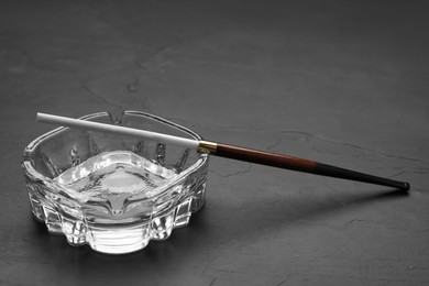Photo of Cigarette in elegant holder and clean glass ashtray on black table