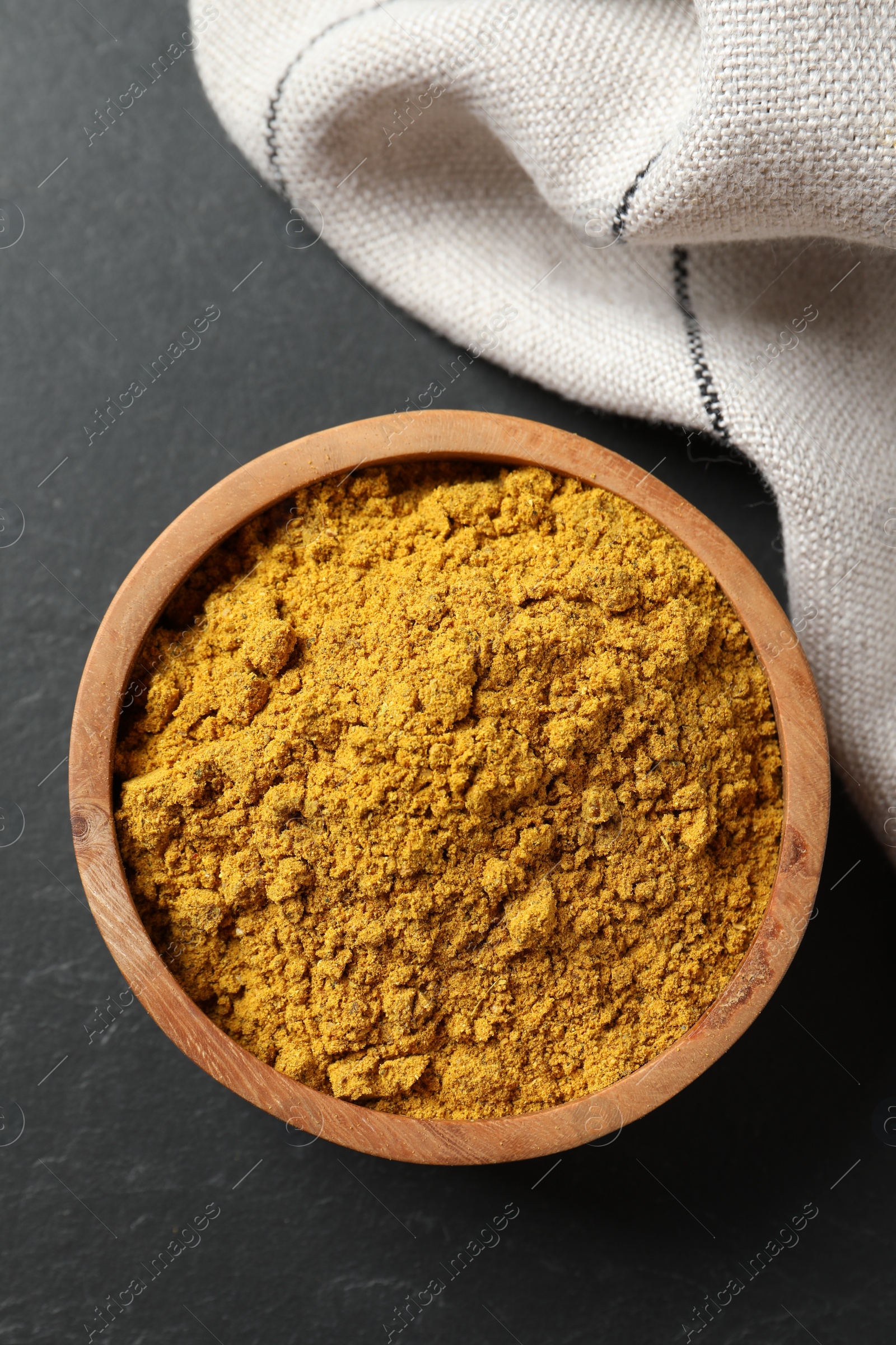 Photo of Dry curry powder in bowl on dark textured table, top view