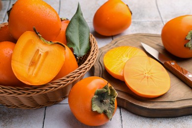 Photo of Delicious ripe juicy persimmons in wicker basket on tiled surface