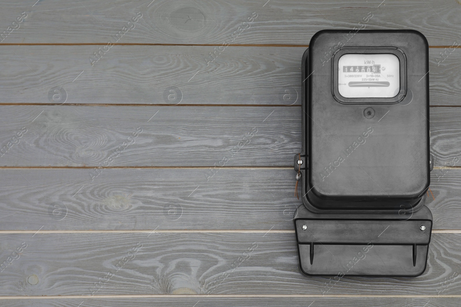 Photo of Black electric meter on grey wooden background, top view with space for text. Measuring device