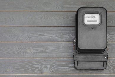 Black electric meter on grey wooden background, top view with space for text. Measuring device