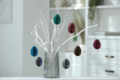 Branches with paper eggs in vase on white table indoors. Beautiful Easter decor