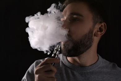 Photo of Man using electronic cigarette on black background