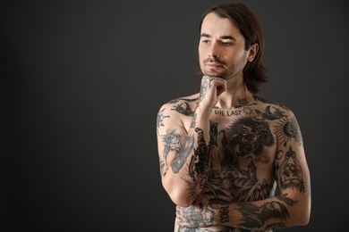Photo of Young man with tattoos on body against black background. Space for text