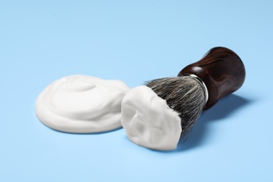 Photo of Brush with shaving foam on light blue background, closeup