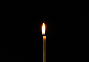 One burning church candle on dark background