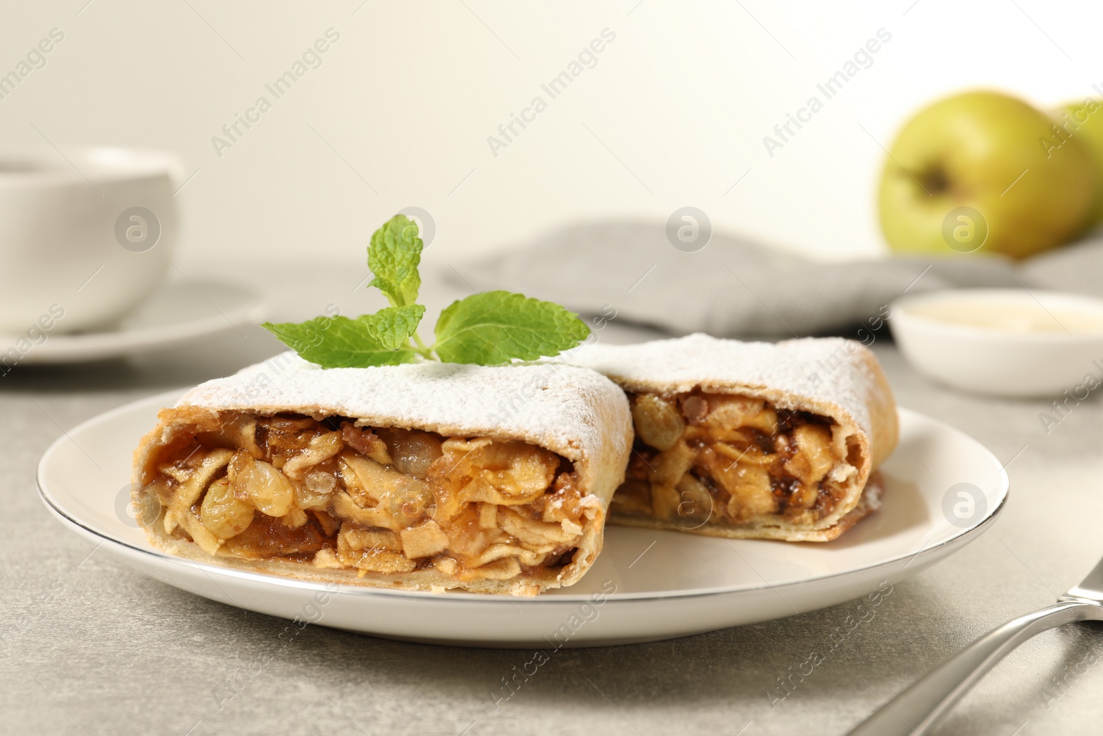 Photo of Delicious strudel with apples, nuts and raisins on light grey table, closeup