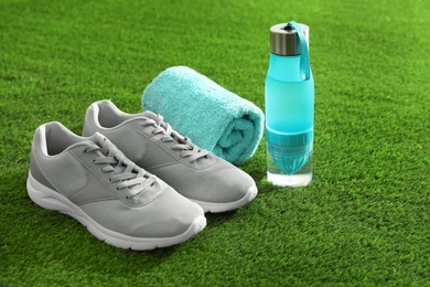 Photo of Bottle of water, sneakers and towel on artificial grass. Fitness equipment