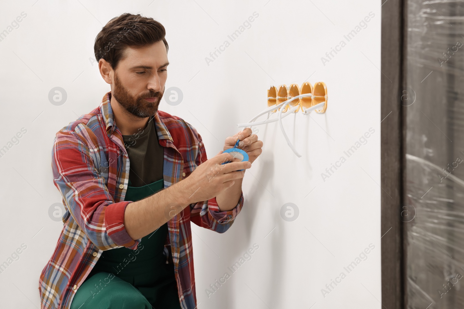 Photo of Electrician fixing wires with insulating tape indoors