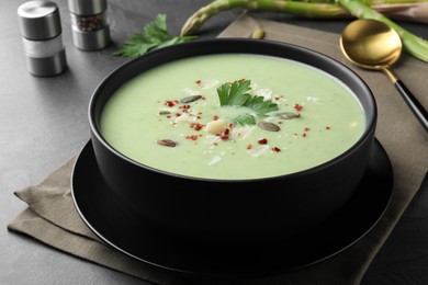 Photo of Bowl of delicious asparagus soup on dark table