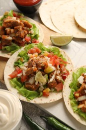 Photo of Delicious tacos with vegetables, meat and lime on grey textured table