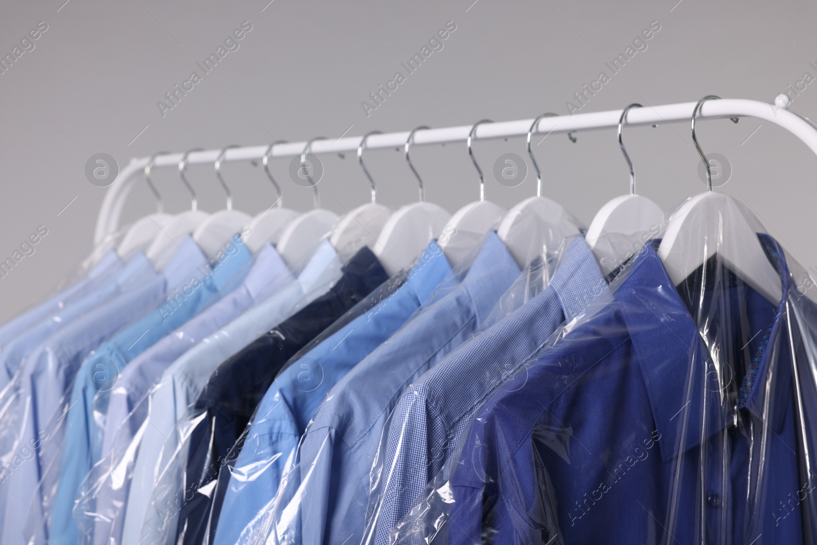 Photo of Dry-cleaning service. Many different clothes in plastic bags hanging on rack against grey background