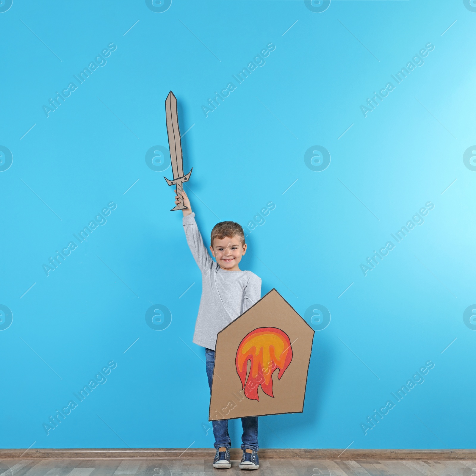 Photo of Cute little boy playing with cardboard sword and shield near color wall. Space for text