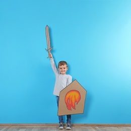 Photo of Cute little boy playing with cardboard sword and shield near color wall. Space for text