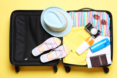 Photo of Open suitcase with beach objects on yellow background, top view