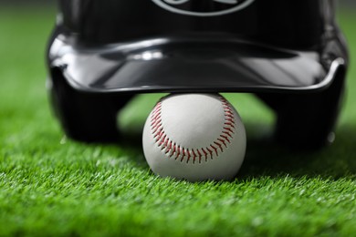 Photo of Batting helmet and baseball ball on green grass, closeup