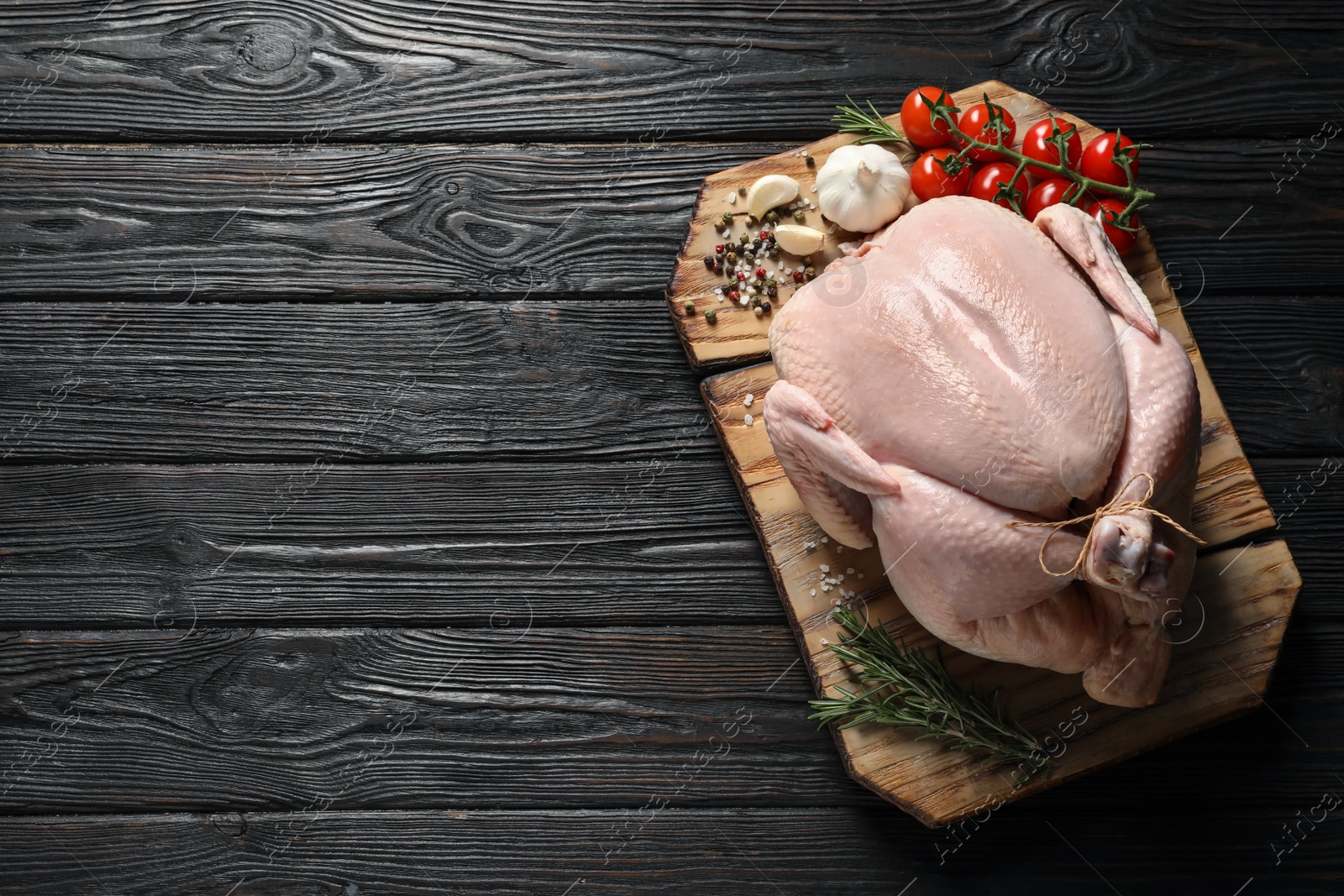 Photo of Board with raw turkey and ingredients on wooden background, top view. Space for text