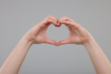 Woman showing heart gesture with hands on grey background, closeup