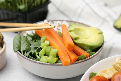 Delicious poke bowl with basil, vegetables and avocado on light grey table, closeup