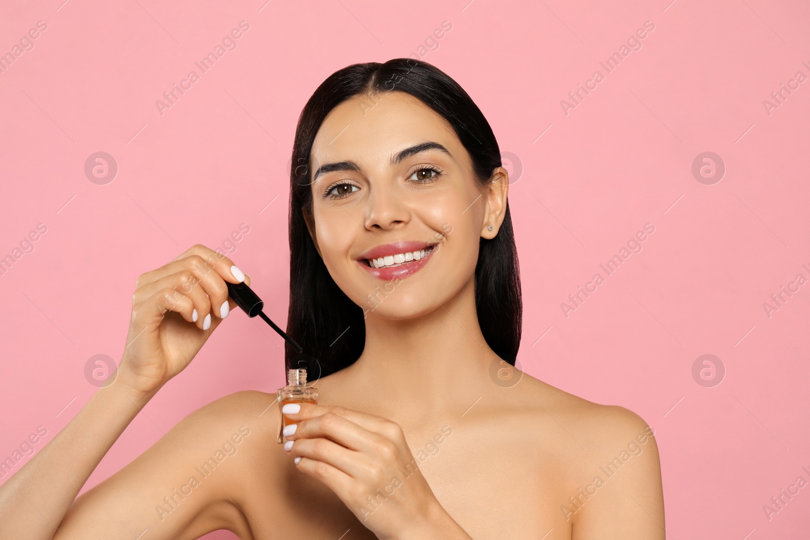 Photo of Young woman with eyelash oil on pink background