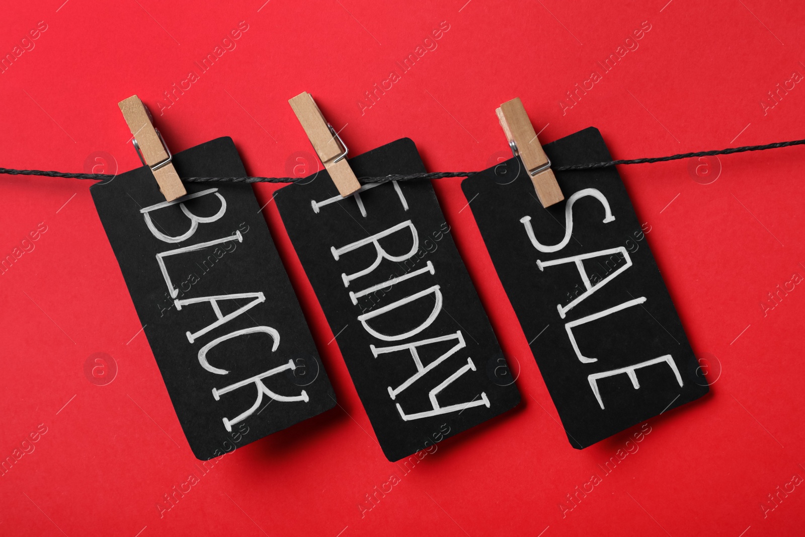 Photo of Tags with words Black Friday Sale on rope against red background