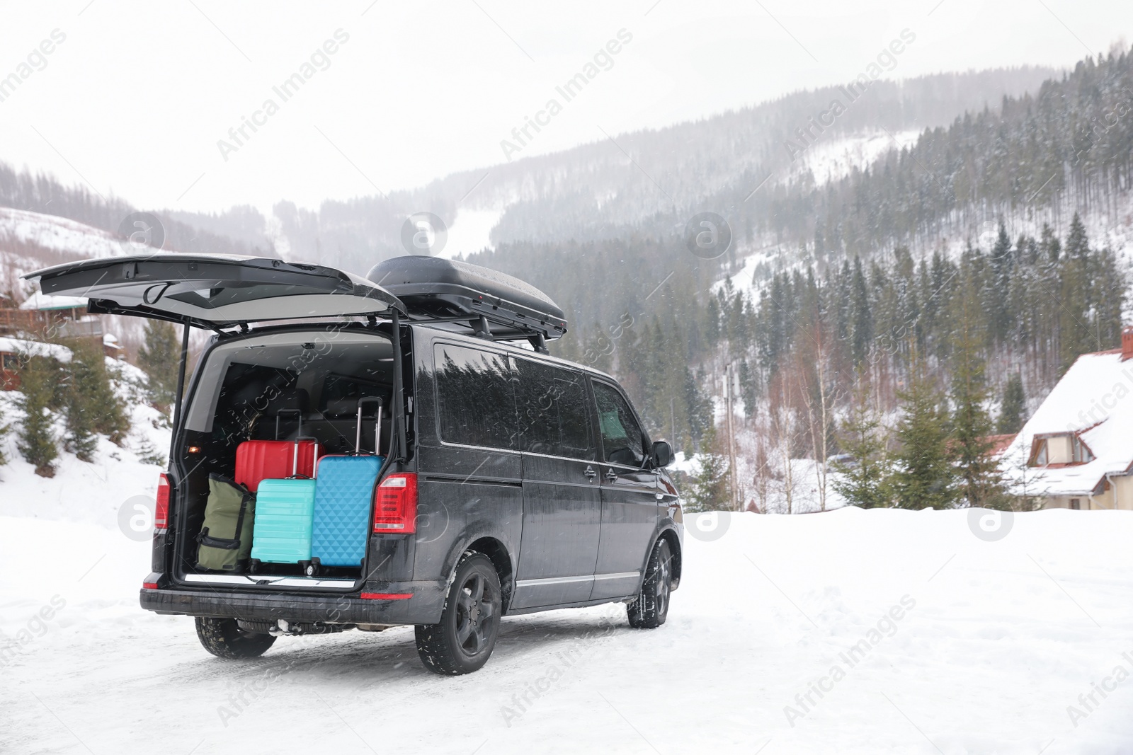 Photo of Black car with luggage in trunk on snowy road. Winter vacation