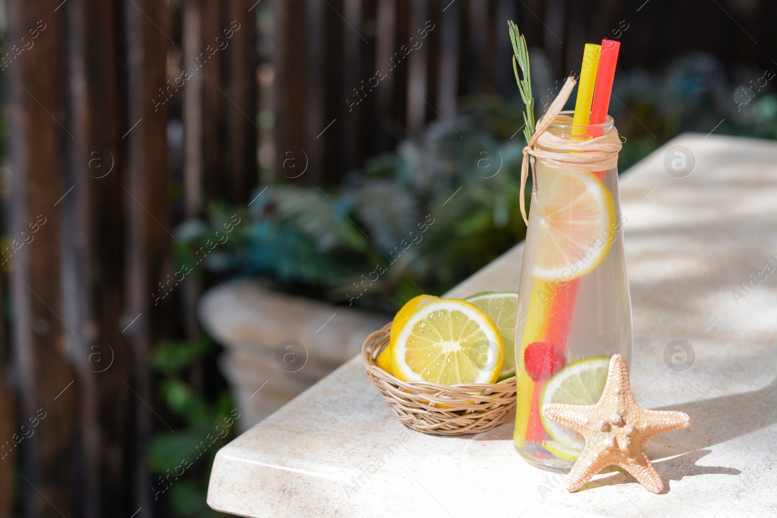 Photo of Refreshing tasty lemonade served in glass bottle and citrus fruits on beige table. Space for text