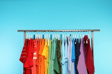 Wardrobe rack with different bright clothes on color background