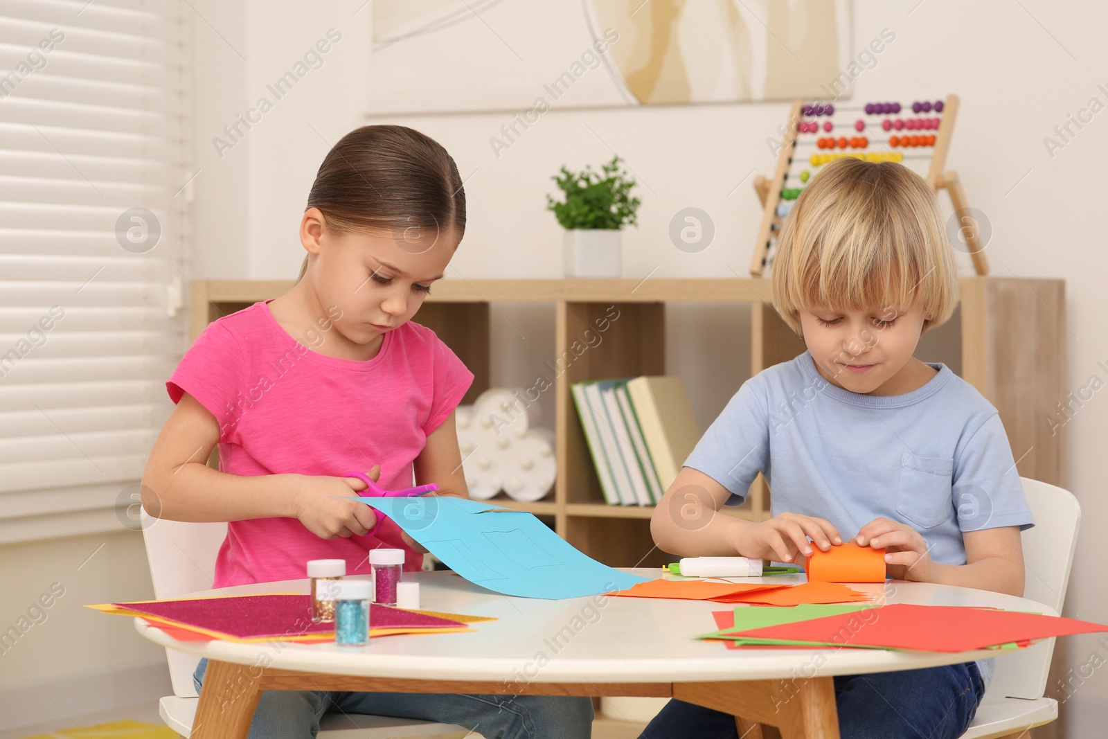 Photo of Cute children cutting colorful paper at desk in room. Home workplace